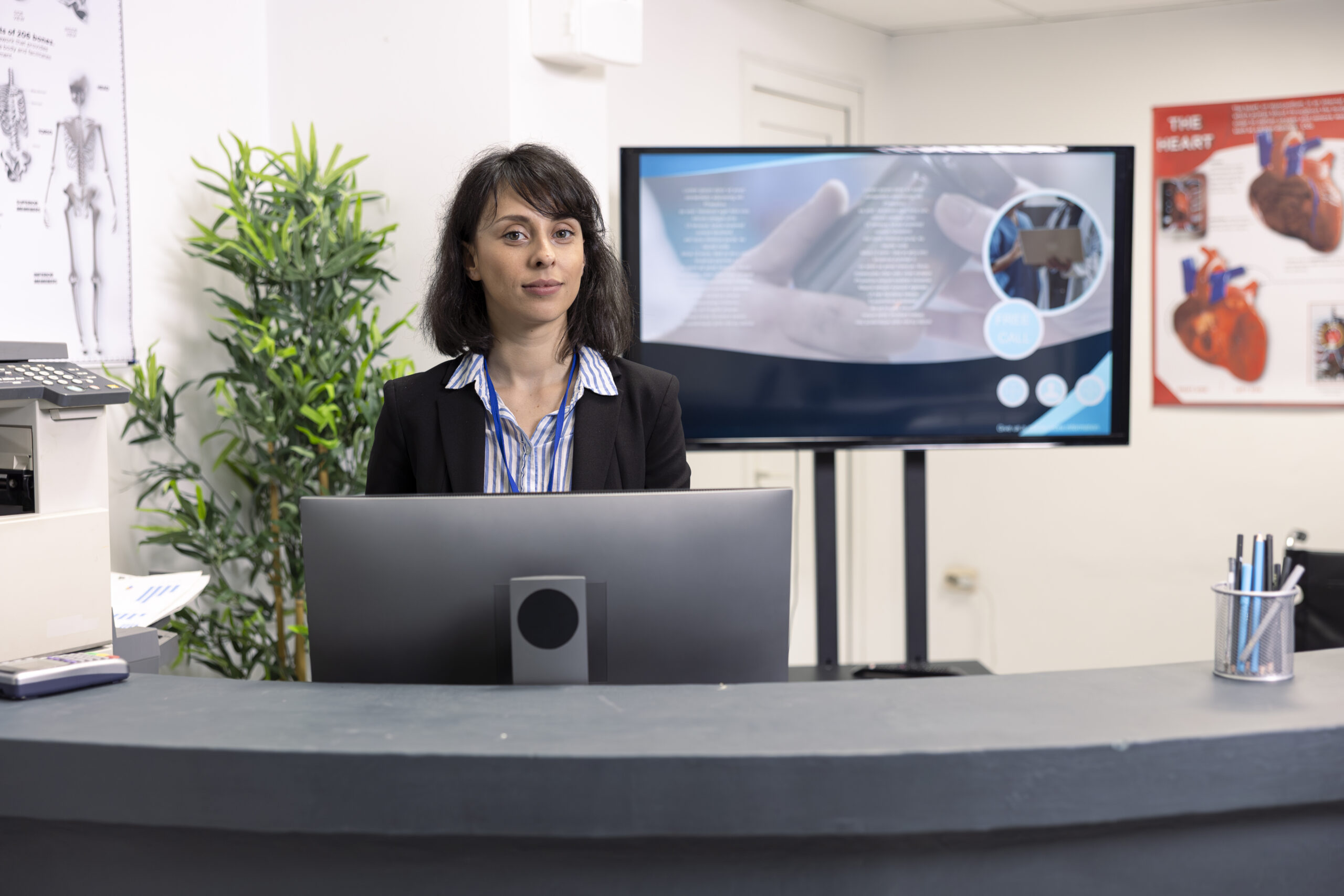 Virtual Medical Receptionist standing at a front desk, assisting patients in a clinic reception area